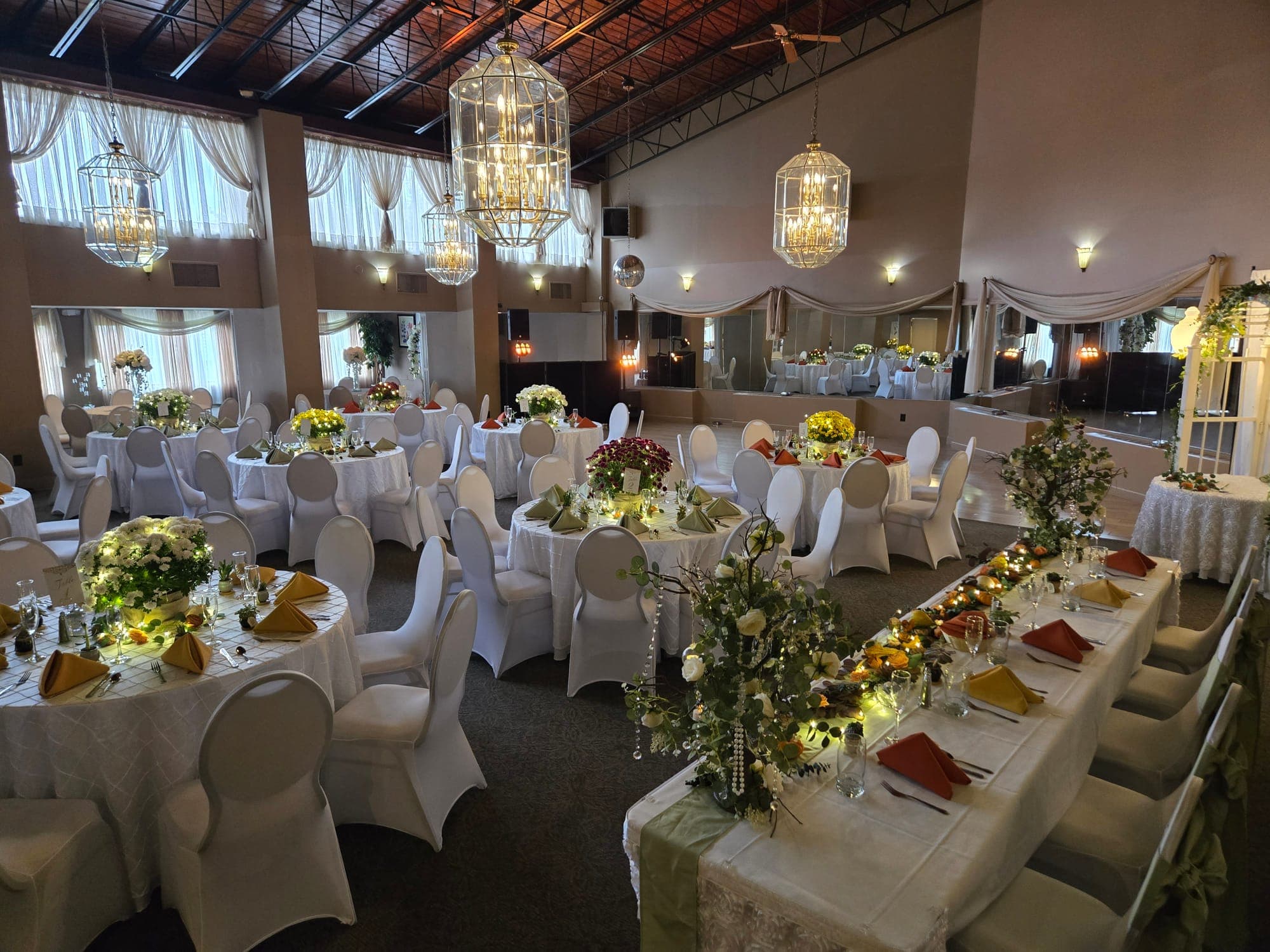 Wedding reception in the Candlelite Room with a long head table of rust and sage napkins under lantern chandeliers and tall draped windows in Delran NJ