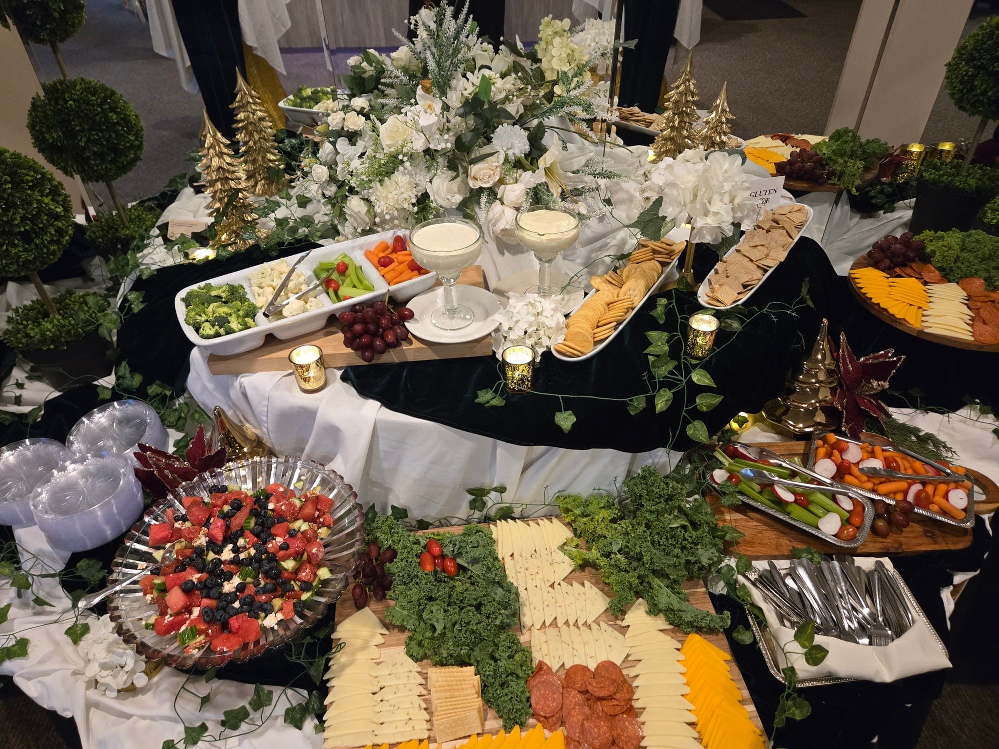 Grazing table with cheese and charcuterie boards, crudités, crackers, dips and a berry bowl among white flowers