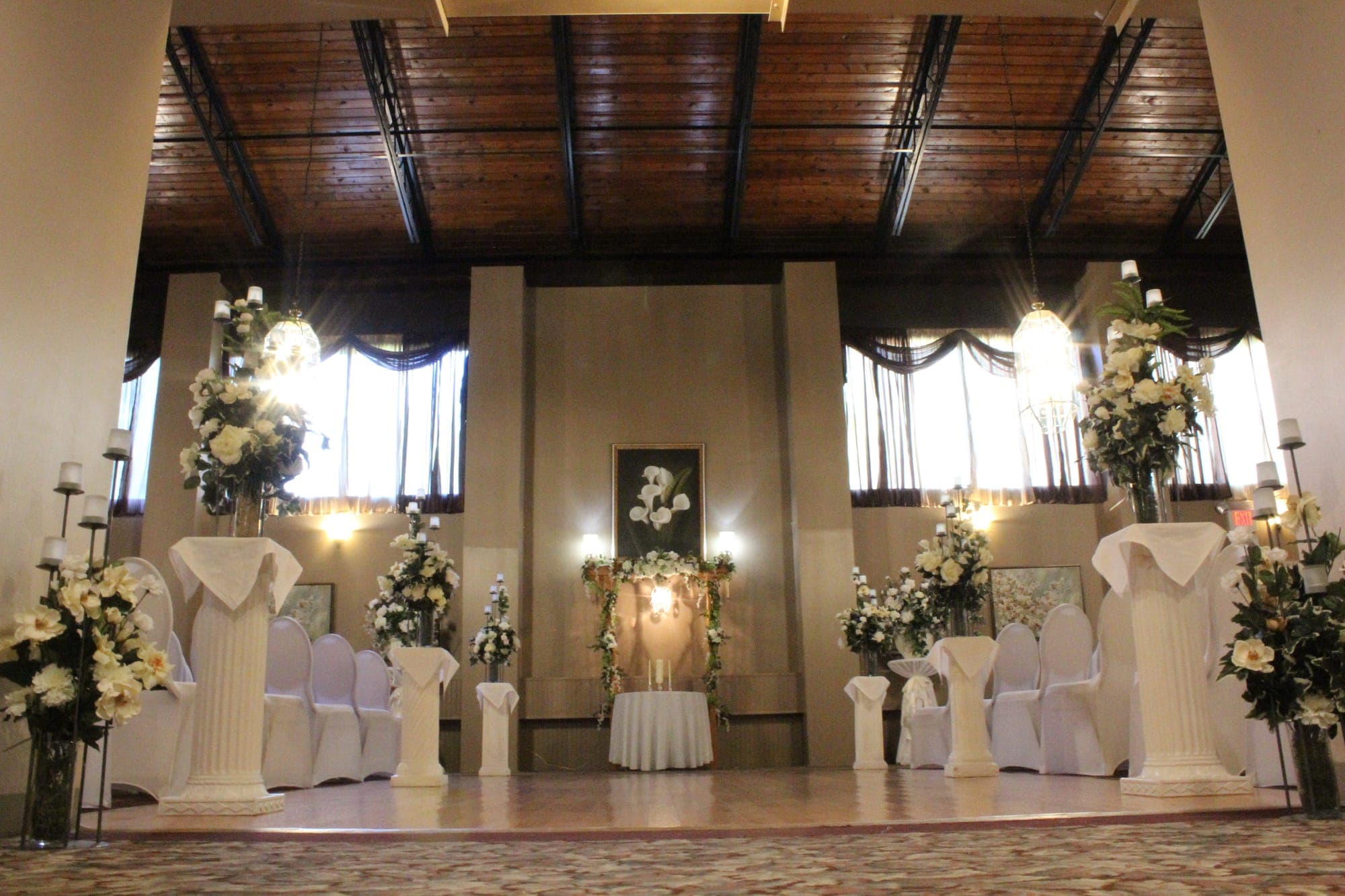 Wedding ceremony setup with white columns, cream floral arrangements, candle stands and a flower-draped arbor