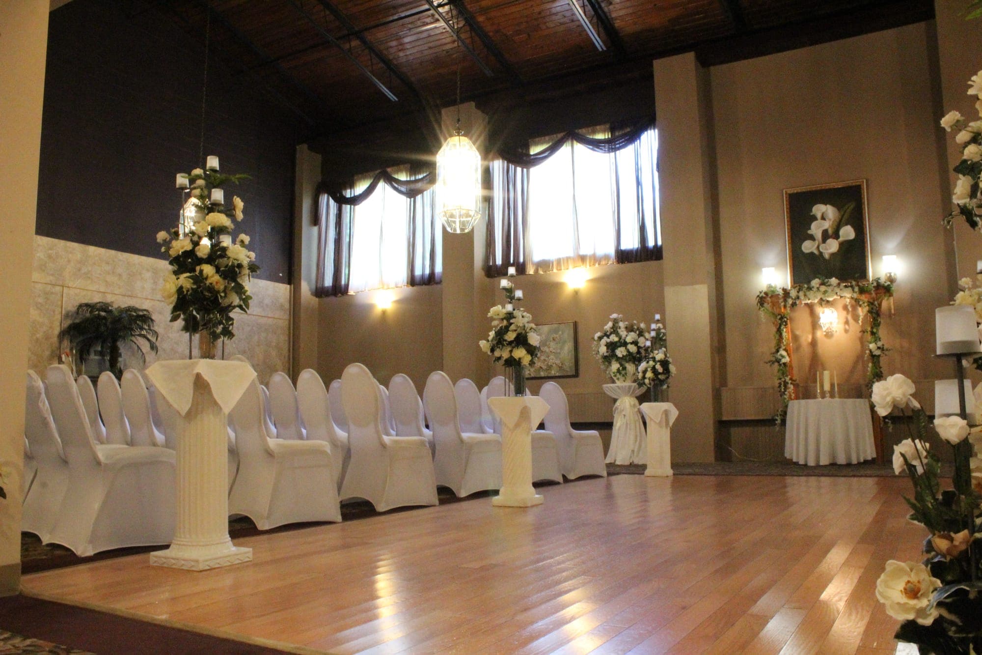 Rows of white-covered ceremony chairs along a wood aisle leading to a floral arbor and unity candle table in Delran NJ