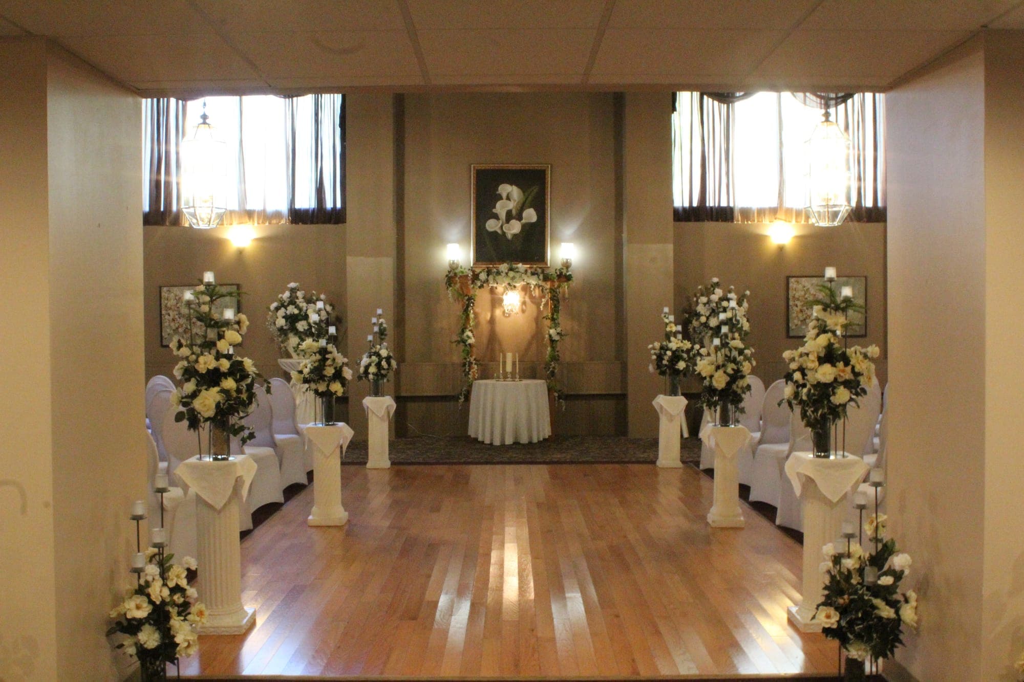 Wood-floor ceremony aisle lined with columns and cream flowers leading to a floral arbor