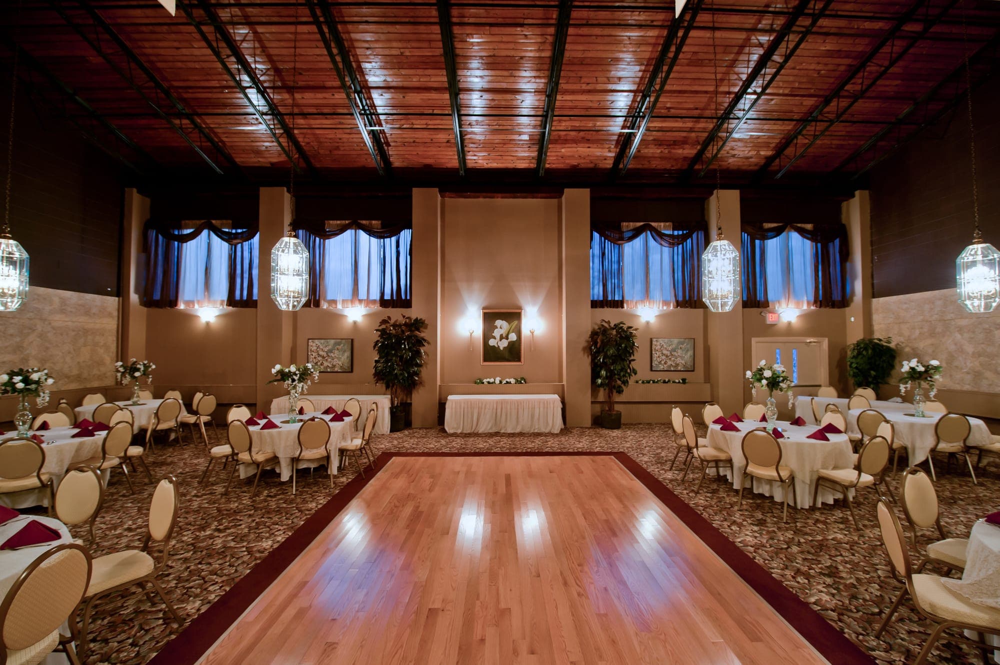 The Garden Room with wood-plank ceiling, lantern chandeliers, central wood dance floor and round tables with burgundy napkins